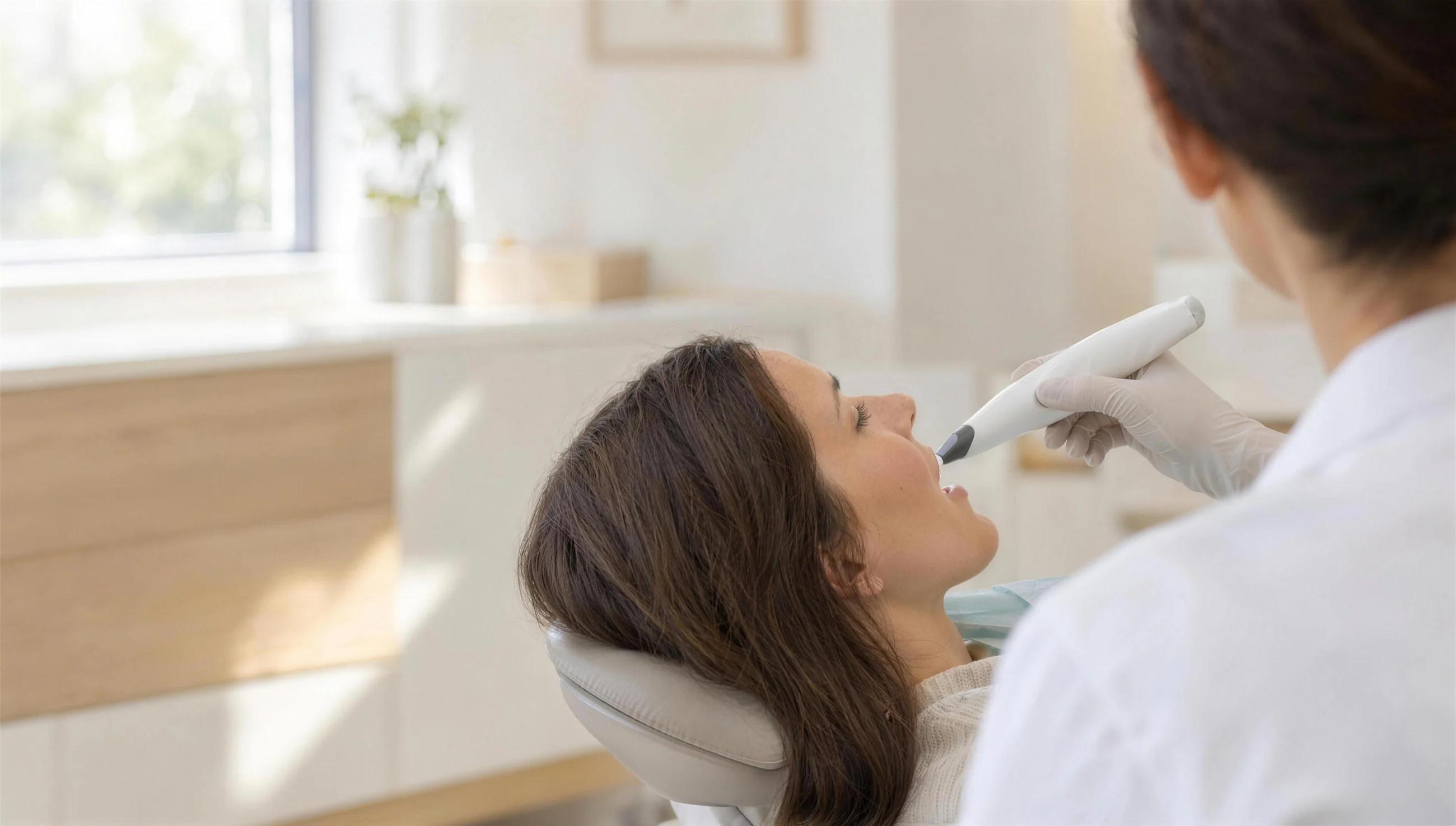 Behandler scannt die Zähne einer Patientin mit dem kabellosen Intraoralscanner, von hinten gesehen